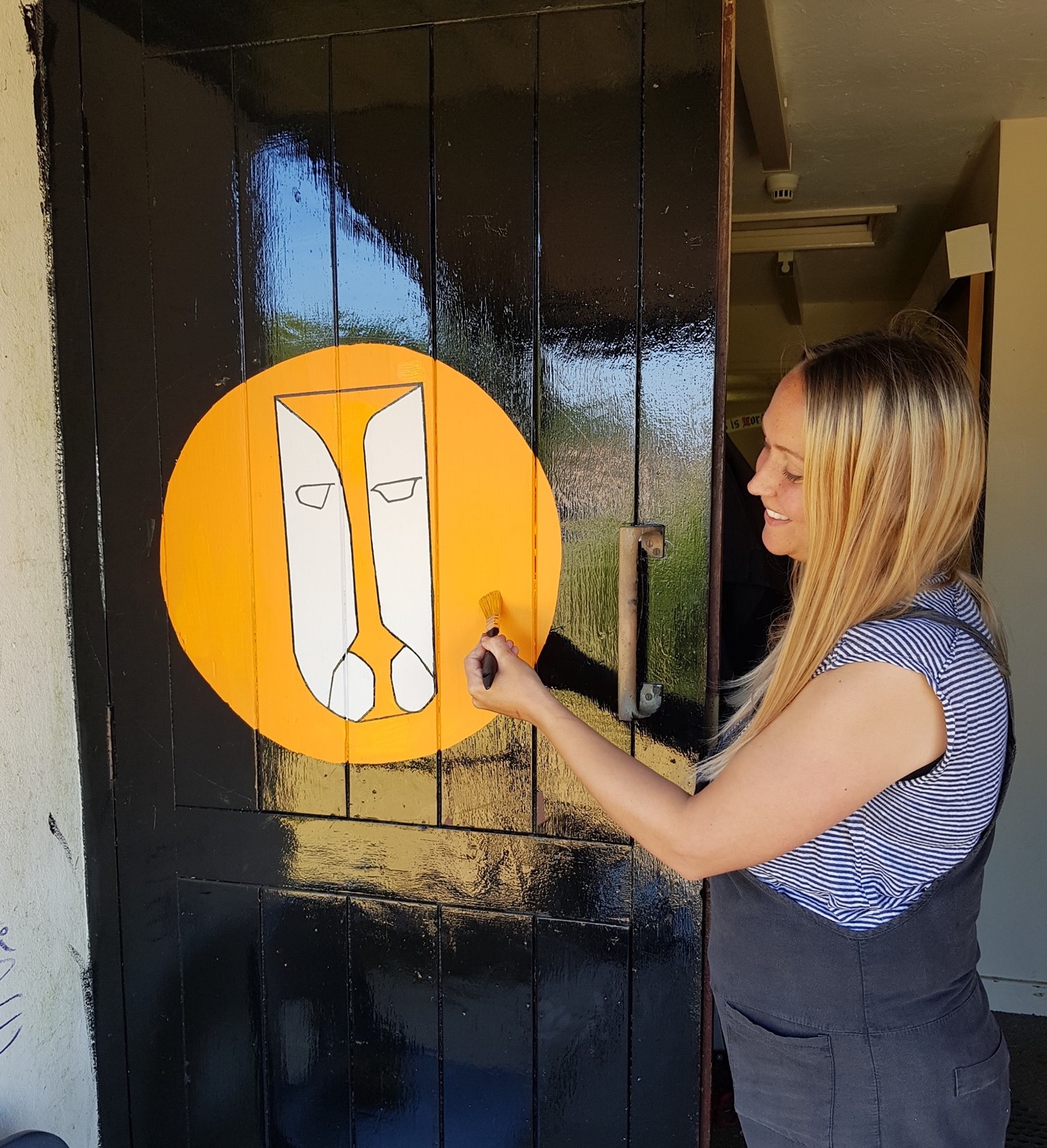 Artist Nicola Parsons painting a yellow sign on a black door