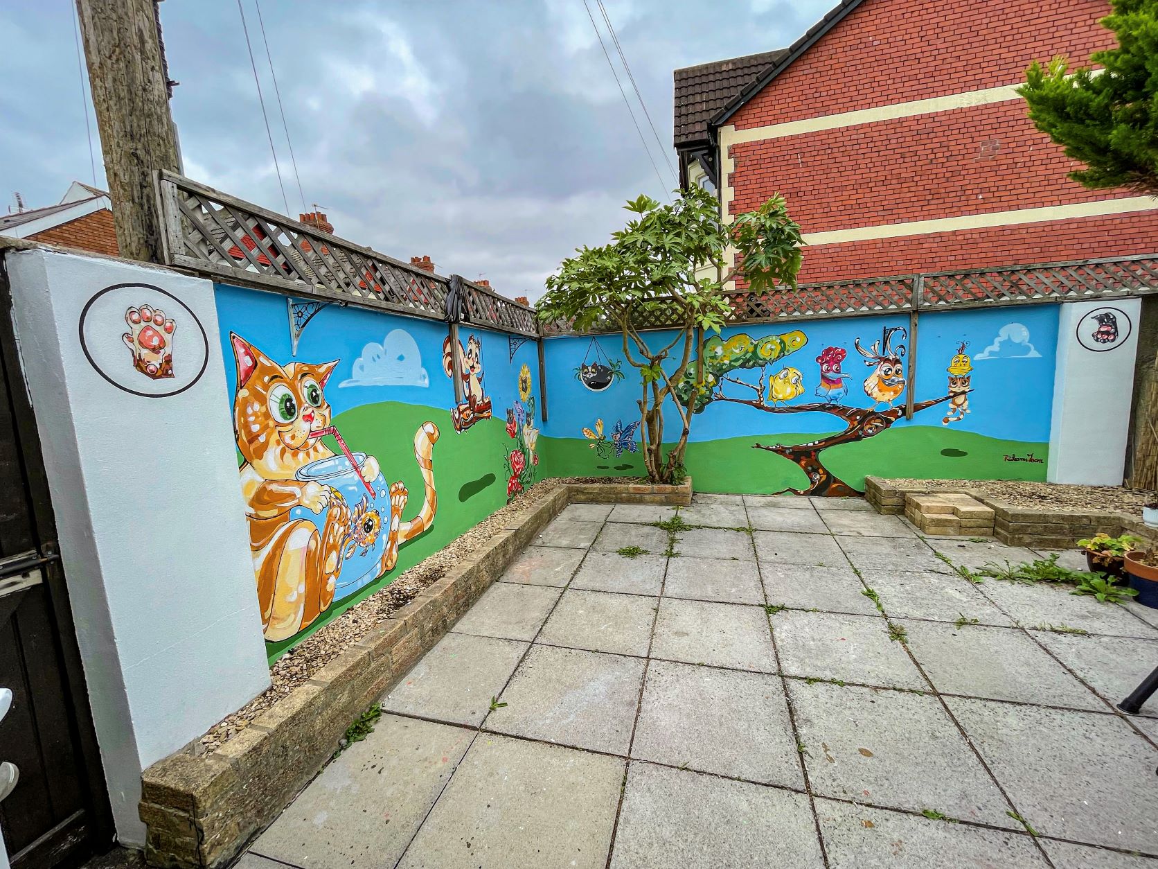 ‘HAPPY GARDEN’ MURAL OUTDOOR ARTWORK - Innovate Trust approached me to develop a mural for a 15m-square garden space – where people living in adjacent supported accommodation could have an input into the themes of the work. The individuals shared their love of cats and birds, and I added a few touches of my own to create a bright, colourful and cheerful scene. The response was very positive: the characters raise a smile even on rainy days and they have been given names! 
